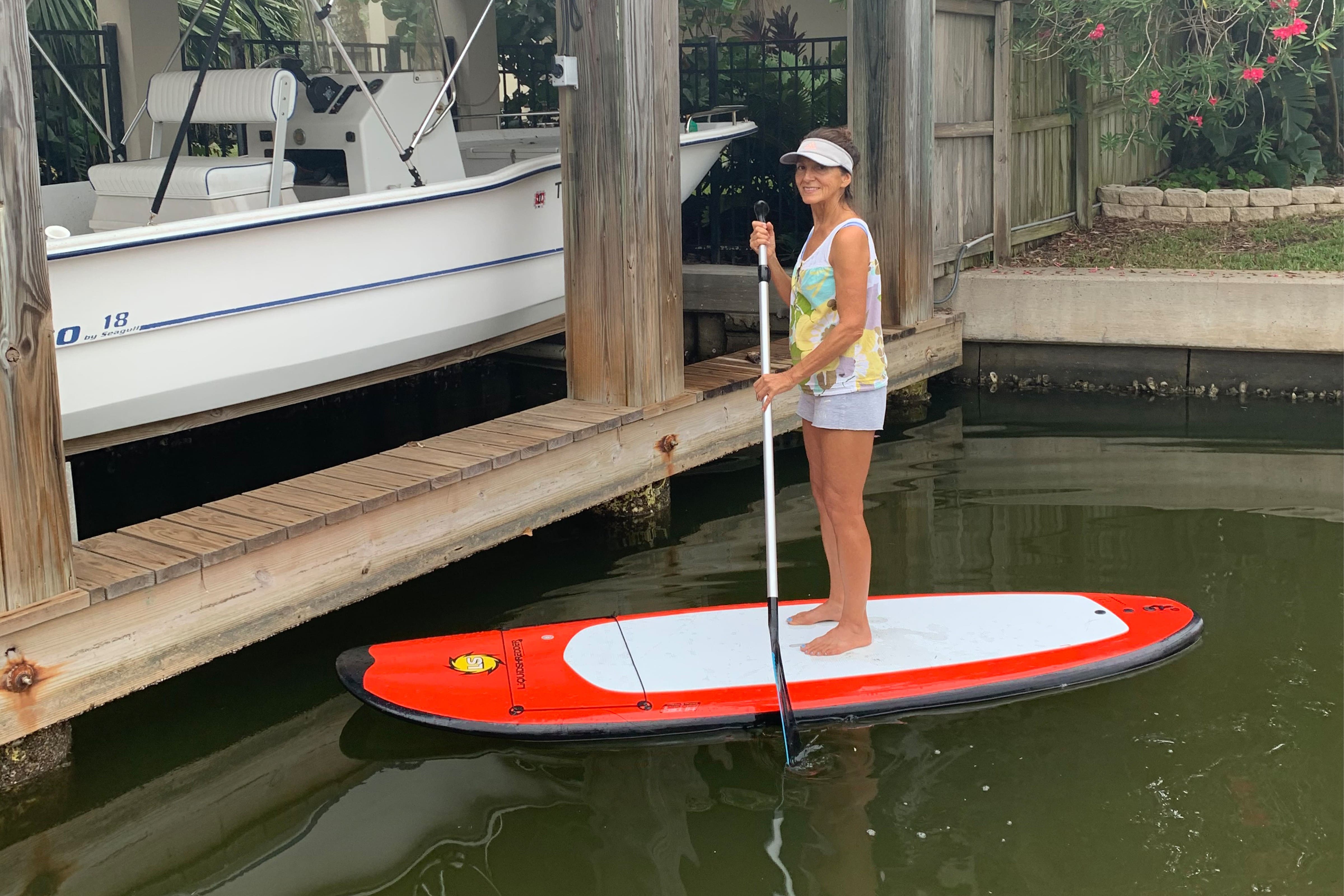 A woman stands confidently on a paddle board, surrounded by calm water